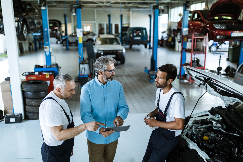 Mid adult manager using touchpad and talking to car mechanics in a workshop.